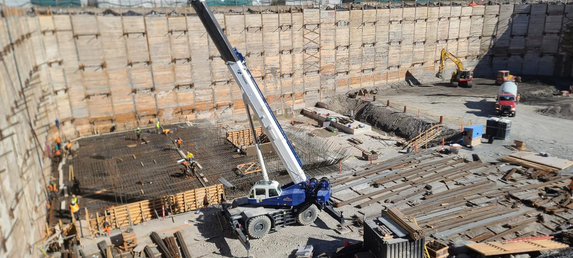 Panoramic deep excavation showing crane placement, working crews, and foundation construction staging