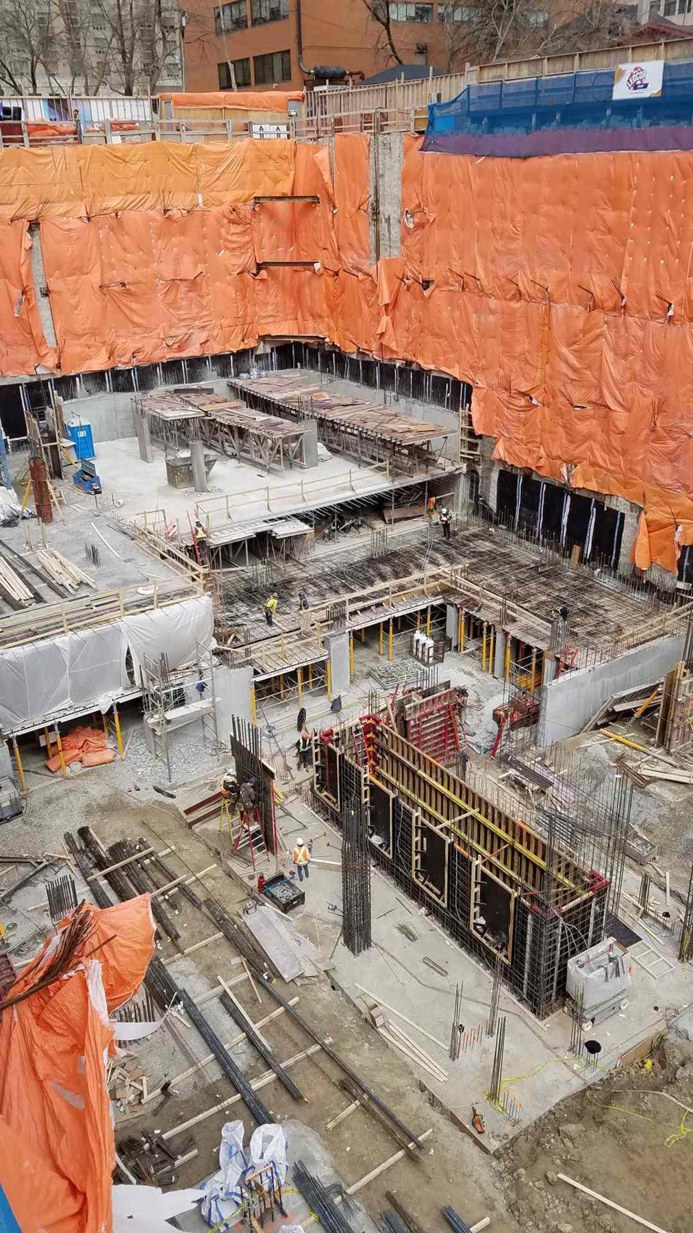 Deep excavation with concrete walls, forming zones, and structural layout work in progress