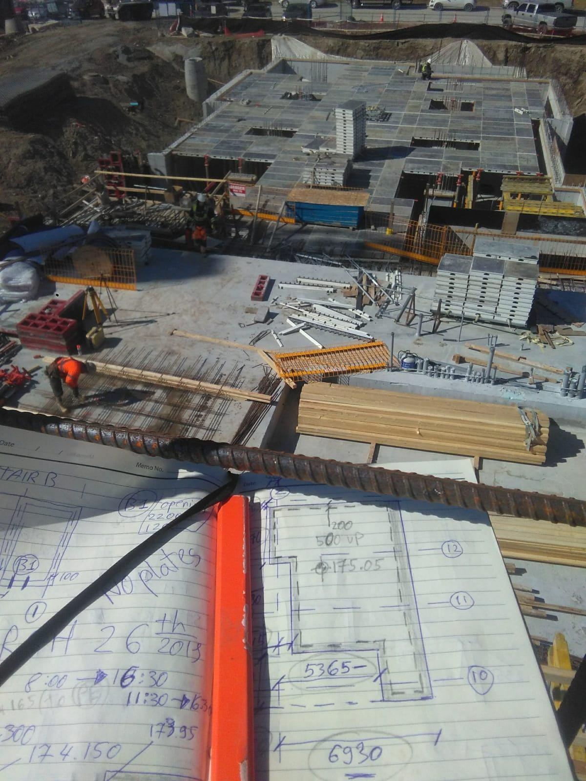 Construction drawings and total station setup overlooking active concrete forming operations
